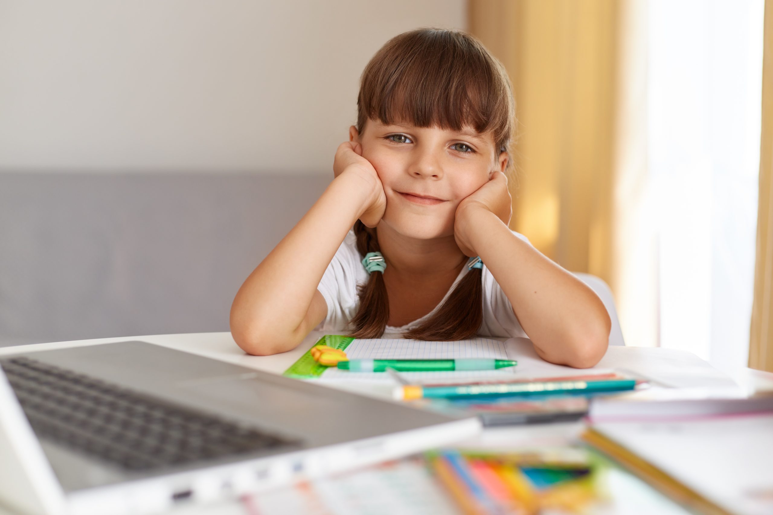 indoor shot happy positive female child looking camera with optimistic facial expression doing homework likes online lessons quarantine scaled
